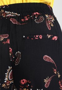 Svart mönstrad tyg med blommönster och paisleymönster i rosa, röd, orange och vitt. Elastisk midja med en liten bakficka.