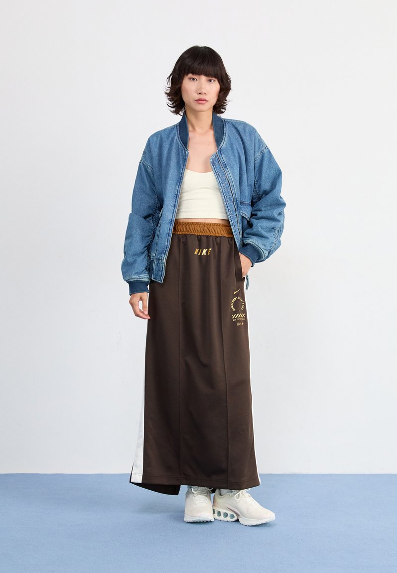 Denim Bomberjacke, weißes Tanktop, brachter Sportrock mit goldenen Akzenten und helle Sneakers. Glatte Texturen und lässiges Design.
