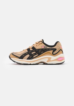 Zapatilla deportiva beige y negra con parte superior de malla, suela acolchada, diseños en negro y acentos rosas en el talón y el logo.