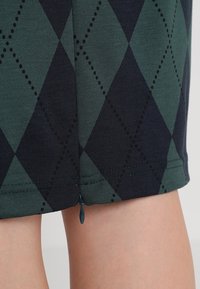 Sukně do délky kolen vyrobená z elastické tkaniny, zdobená tmavě zeleným a námořnickým argyle vzorem, s černými tečkovanými akcenty a malým zipem.