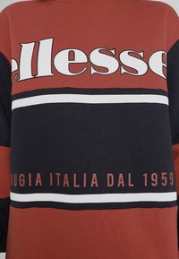 Czerwony i granatowy sweatshirt z dużym białym logo "ellesse", poziomymi paskami i napisem "RUGIA ITALIA DAL 1959" w ciemnoczerwonym kolorze. Miękka faktura materiału.