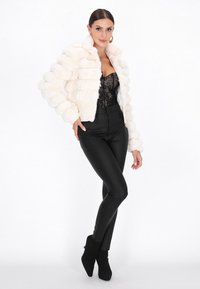 Giacca corta in pelo finto bianco con strisce orizzontali puffate, chiusura con zip e colletto alto, abbinata a pantaloni neri aderenti e stivali alla caviglia.