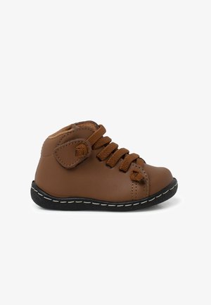 Hnědá kožená kotníková bota s elastickými šněrovadly, polstrovaným límcem a černou gumovou podrážkou. Disponuje hladkým povrchem a kontrastními švy.