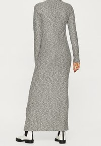 Maxikleid aus grauem Rippstrickmaterial, taillierter Schnitt, hoher Kragen, lange Ärmel und einfarbiges Muster. Kombiniert mit schwarz-weißen Stiefeletten.
