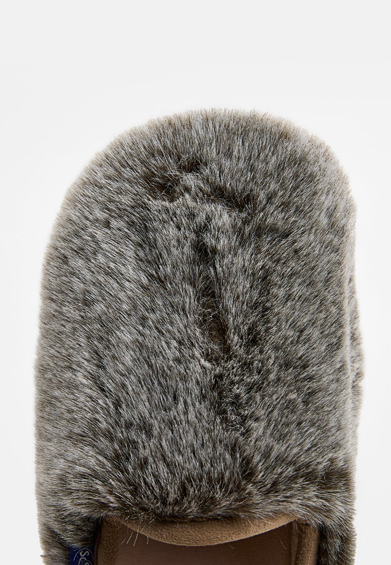 Chausson en fausse fourrure grise avec un dessus arrondi, texture douce et base beige. Présente une petite ouverture à l'avant pour permettre une meilleure circulation de l'air.