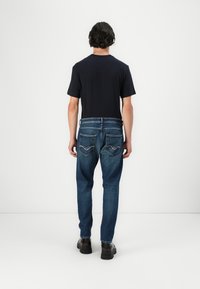 Dark navy t-shirt paired with light blue denim jeans featuring back pockets and contrasting stitching. The model wears black shoes.