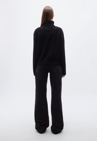 Pull à col roulé en tricot noir avec une texture côtelée, associé à un pantalon noir taille haute à jambes larges. Design minimaliste, sans motifs ni détails visibles.