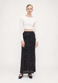 Witte lang Mouwen crop top gecombineerd met een zwarte pailletten lange rok; de rok heeft een gestructureerd oppervlak met glinsterende accenten en een aansluitende taille.