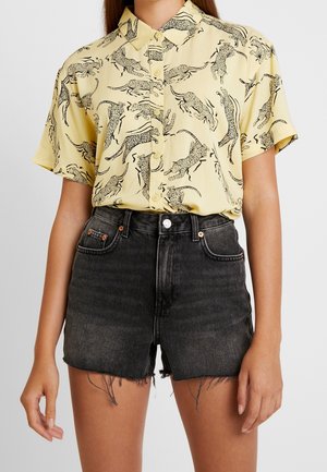 Chemise jaune à manches courtes avec imprimé léopard noir et devant boutonné, associée à un short en denim noir avec ourlets effilochés et poches.