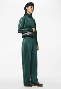 Grøn satin træningsdragt med hvide accenter, parret med en sort crossbody taske med firkantet lukning og tekstureret design, båret med sorte sko.