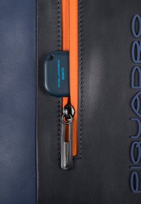 Borsa in pelle con sezioni blu navy e nera, una cerniera arancione, hardware metallico e un'etichetta blu con la scritta "PIQUADRO BAGMATIC."