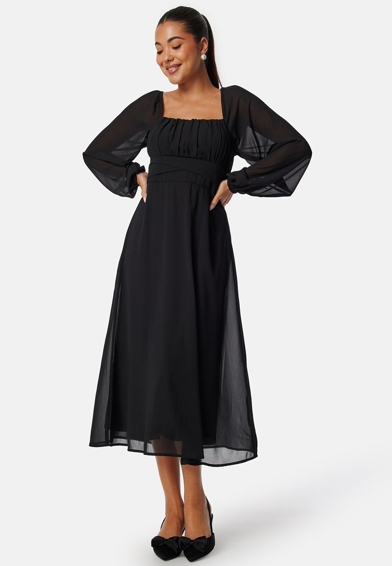 Abito maxi nero con lunghe maniche a sbuffo trasparenti, scollatura quadrata e dettagli arricciati sul corpetto. Tessuto fluente con una leggera lucentezza.