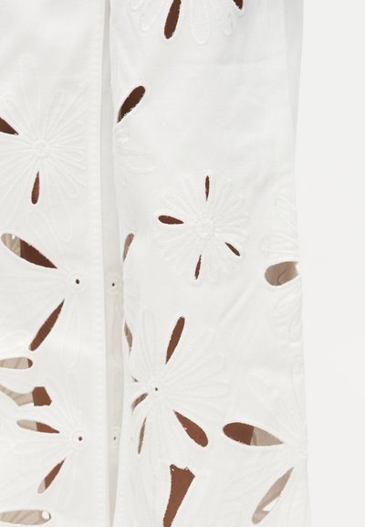 Λευκό ύφασμα με μεγάλα κεντημένα ανθικά κοψίματα και οπές σε σχήμα πέταλου, παρουσιάζοντας λεπτομερείς ραφές και υφή σχεδίασης.