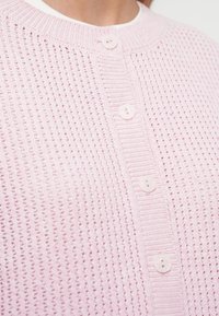 Ροζ πλεκτή ζακέτα με υφασμάτινο μοτίβο, στρογγυλή λαιμόκοψη και τρία ταιριαστά κουμπιά μπροστά.