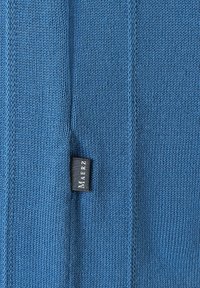 Modrý pletený oděv s texturovaným povrchem, který má malou černou značkovou etiketu. Tkanina vykazuje těsné a rovnoměrné vzorování.