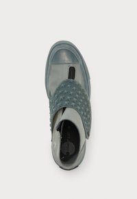 Sapato cinza de deslizar com uma sobreposição de borracha texturizada e pontiaguda, biqueira suave, elástico lateral preto e logotipo circular na palmilha.