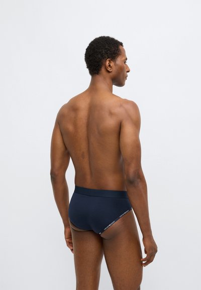 Tumši zils kokvilnas apakšbikses ar elastīgu jostu. Minimālistisks dizains, gluda tekstūra, uz jostas ir zīmola logotips.