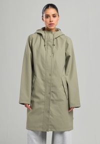 Vaalean ruskea sadetakki, jossa on huppu, napit, sivutaskut ja rento istuvuus. Sujuva pinta, keskikohdan pituus, kestävä materiaali.