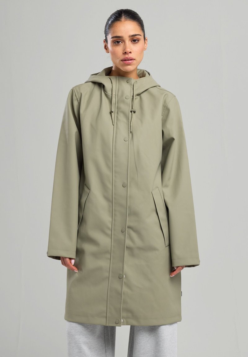 Vaalean ruskea sadetakki, jossa on huppu, napit, sivutaskut ja rento istuvuus. Sujuva pinta, keskikohdan pituus, kestävä materiaali.