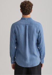 Camicia blu a maniche lunghe realizzata in tessuto leggero, con colletto con bottoni, cucitura centrale sul retro e polsini con bottoni.