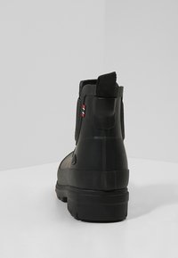 Bota negra impermeable con un acabado texturizado, paneles laterales elásticos y un lazo trasero para facilitar el uso. Suela de goma gruesa para un mejor agarre.