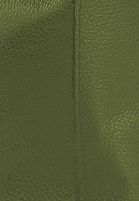 Getextureerd donkergroen leer met een licht korrelige structuur. Zichtbare stiksel details langs een naad, die de duurzaamheid van het materiaal verhogen.