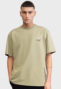 Olijfgroene T-shirt van katoen, met een ronde hals, korte mouwen en een klein logo op de linkerborst gedrukt.