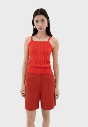 Débardeur en tricot côtelé rouge avec des bretelles larges, associé à un short plissé rouge. Les deux pièces présentent une texture lisse et une coupe ajustée.