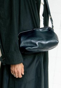 Borsa a mano in pelle nera con una forma morbida e arrotondata e una leggera lucentezza. Presenta una chiusura semplice e una tracolla corta.