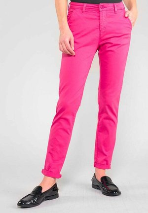 Pantalons en coton rose ajustés avec des ourlets retroussés, dotés d'une fermeture à bouton à l'avant et de poches. Portés avec des mocassins noirs brillants.