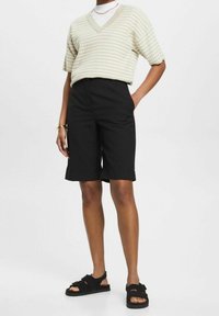 Haut à manches courtes en maille avec motif vert clair et blanc, col en V, associé à un short noir arrivant aux genoux et des sandales noires. Look décontracté et élégant.