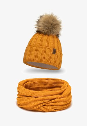 Keltainen neulepipo, jossa on tekoturkis pom-pom ja siihen sopiva infinity-huivi. Molemmissa on ribbikuviointi ja pehmeä vuori.