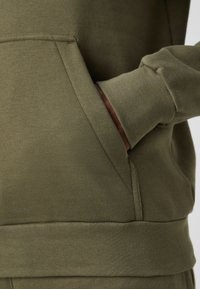 Felpa verde oliva con tasca frontale, polsini e orlo a costine. Realizzata in tessuto morbido, presenta una texture liscia e cuciture pulite.