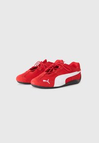 Scarpe da ginnastica rosse con finitura in rete e suede, caratterizzate da un logo bianco sul lato e una suola nera. Design con lacci e forma a profilo basso.
