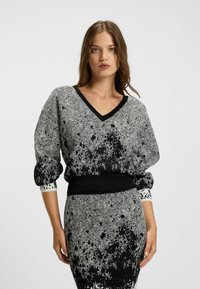 Schwarzer undweißer Strickpullover mit V-Ausschnitt, Hahnentrittmuster, puffierten Ärmeln und einem gerippten Bündchen. Strukturierter Stoff mit Spritzakzenten.