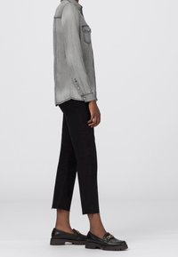 Gray denim shirt with two chest pockets, black cropped jeans with frayed hem, and black loafers with gold accent detail.