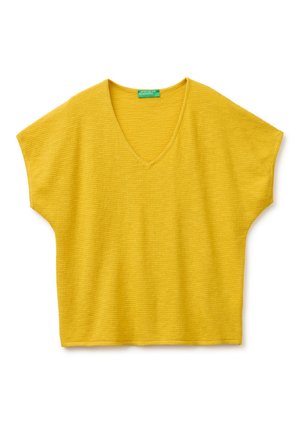 Żółta krótka dzianinowa bluzka z dekoltem w serek i szerokim fasonem na ramionach, ułożona płasko na białym tle.