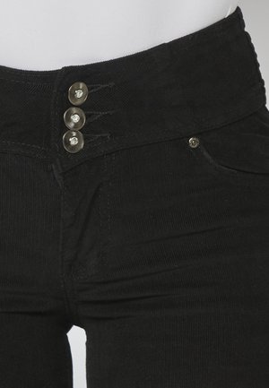 Un pantalon en velours côtelé noir présente une taille haute avec trois boutons en métal décoratifs et une petite poche avant, mettant en valeur une texture côtelée.