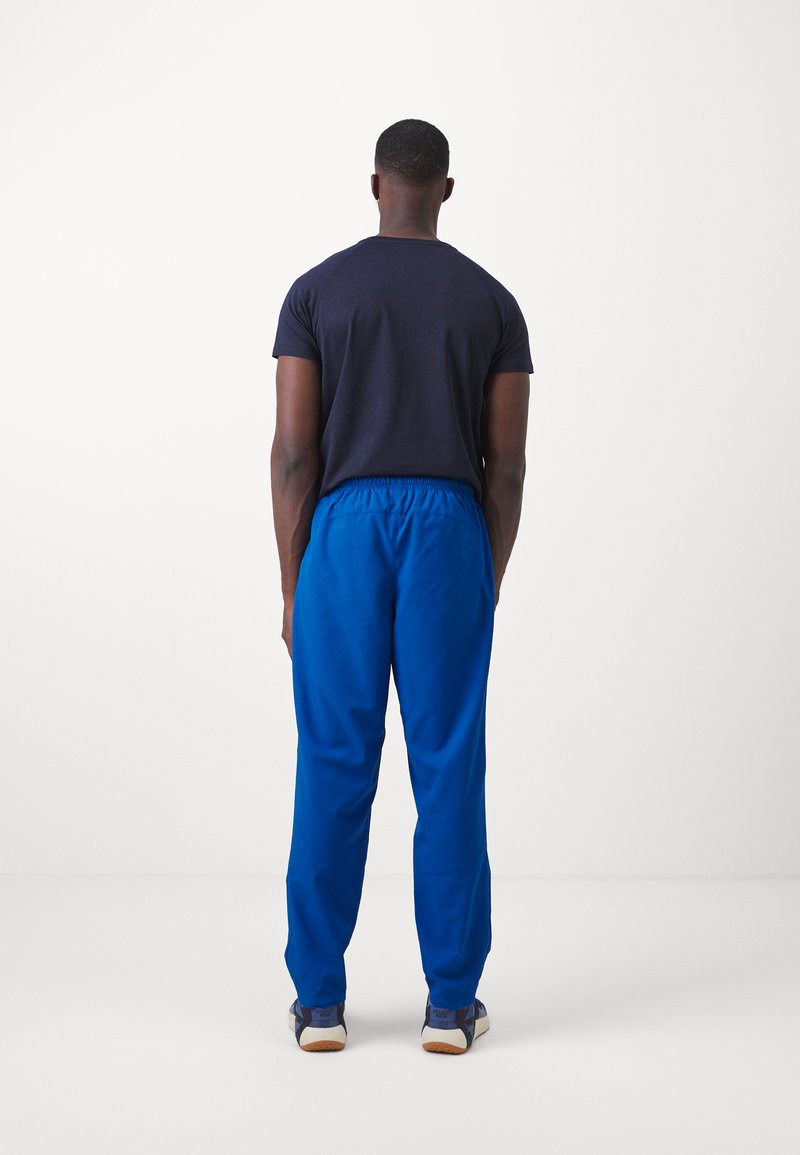 Camiseta de manga corta en color azul marino y pantalones elásticos azules, de tejido suave, corte relajado, combinados con zapatillas oscuras que tienen suelas claras.