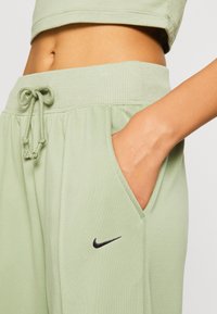 Světlé zelené joggingové kalhoty s elastickým pasem, šňůrkou, kapsami a černým logem Nike na boku. Měkká, hladká bavlněná směs.