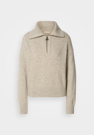 Beige gestrickter Pullover mit hohem Kragen, Reißverschluss und gerippten Bündchen und Saum. Die Textur weist Stellen dunklerer Fasern auf.