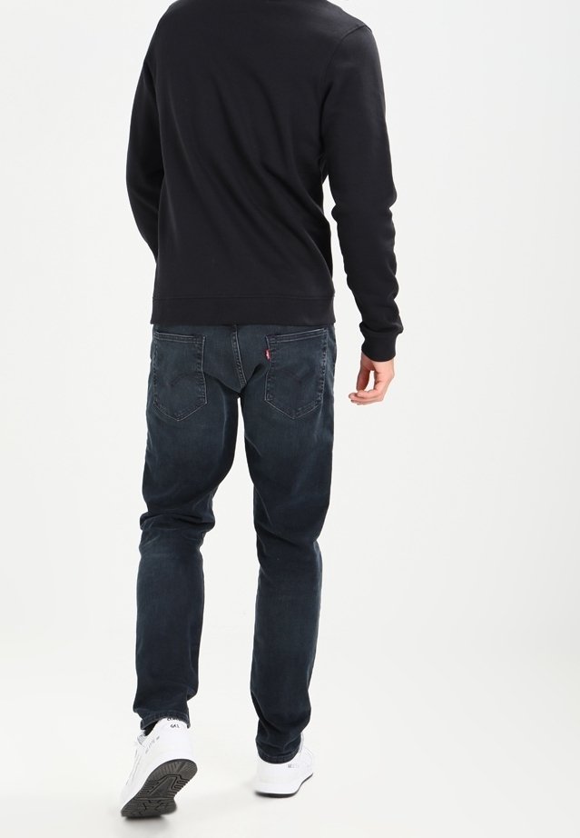 Jeans blu scuro con vestibilità regolare, cinque tasche e lavaggio sbiadito. Abbinati a una felpa nera e sneakers bianche.