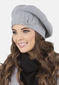 Berete de punto gris con tres acentos de flores texturizadas y perlas. El diseño tiene una forma suave y holgada, y una textura cálida y suave.