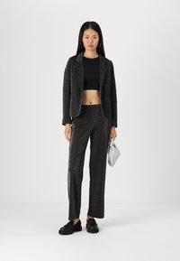 Costume noir texturé avec une veste ajustée et un pantalon large. Porté avec un top court et des chaussures noires, tenant un sac à main en argent.