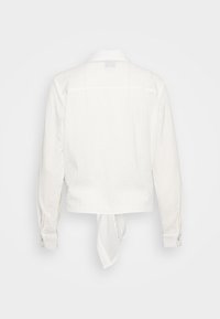 Camisa blanca cortada hecha de tela texturizada, con cuello de punta, mangas largas y un detalle atado en la parte posterior con puños abotonados.