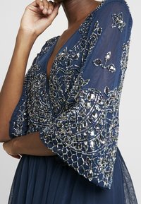 Vestido azul marino con intrincados bordados de cuentas plateadas, diseños florales y mangas anchas. Fabricado en una tela ligera con una silueta fluida.