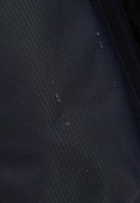 Tessuto nero impermeabile con superficie texturizzata, caratterizzato da piccole gocce d'acqua sul materiale.
