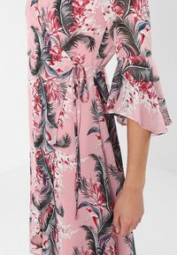 Kwiatowa sukienka z dekoltem w kształcie litery V w kolorze różowym, z czarnymi i czerwonymi wzorami botanicznymi. Posiada dzwonkowe rękawy oraz talię związaną w pasie. Miękka faktura materiału.