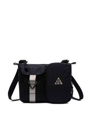 Black crossbody bag with adjustable strap, dual front pockets—one mesh with buckle, one solid with triangular logo.