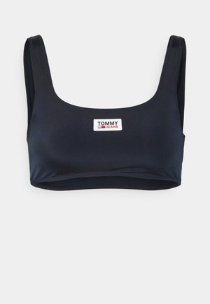 Soutien-gorge de sport court bleu marine en tissu lisse, avec des bretelles épaisses et un logo Tommy Jeans en blanc et rouge sur le devant.